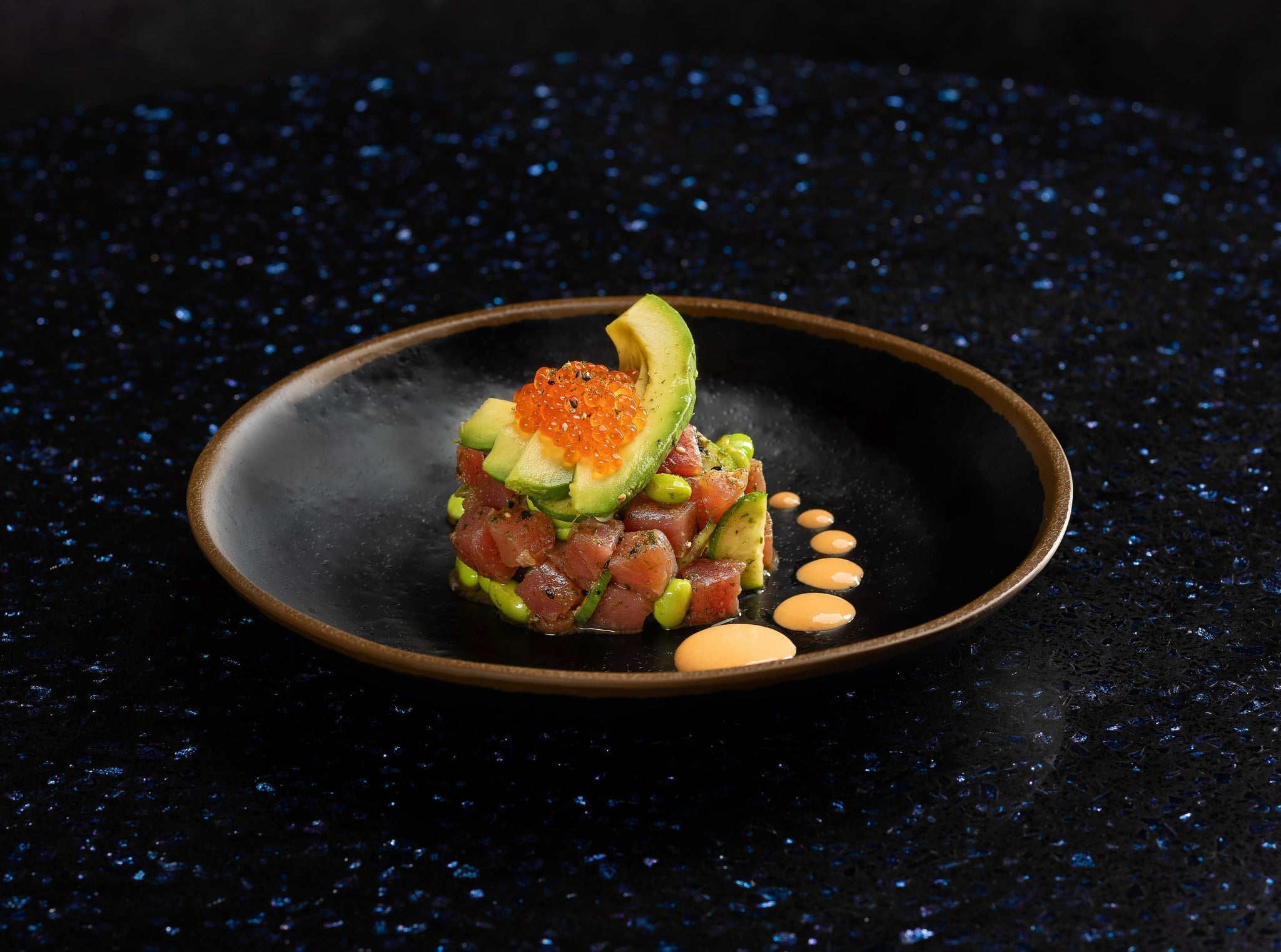 Crispy rice cubes topped with marinated tuna, avocado, and trout roe, served as a bite-sized gourmet appetizer.