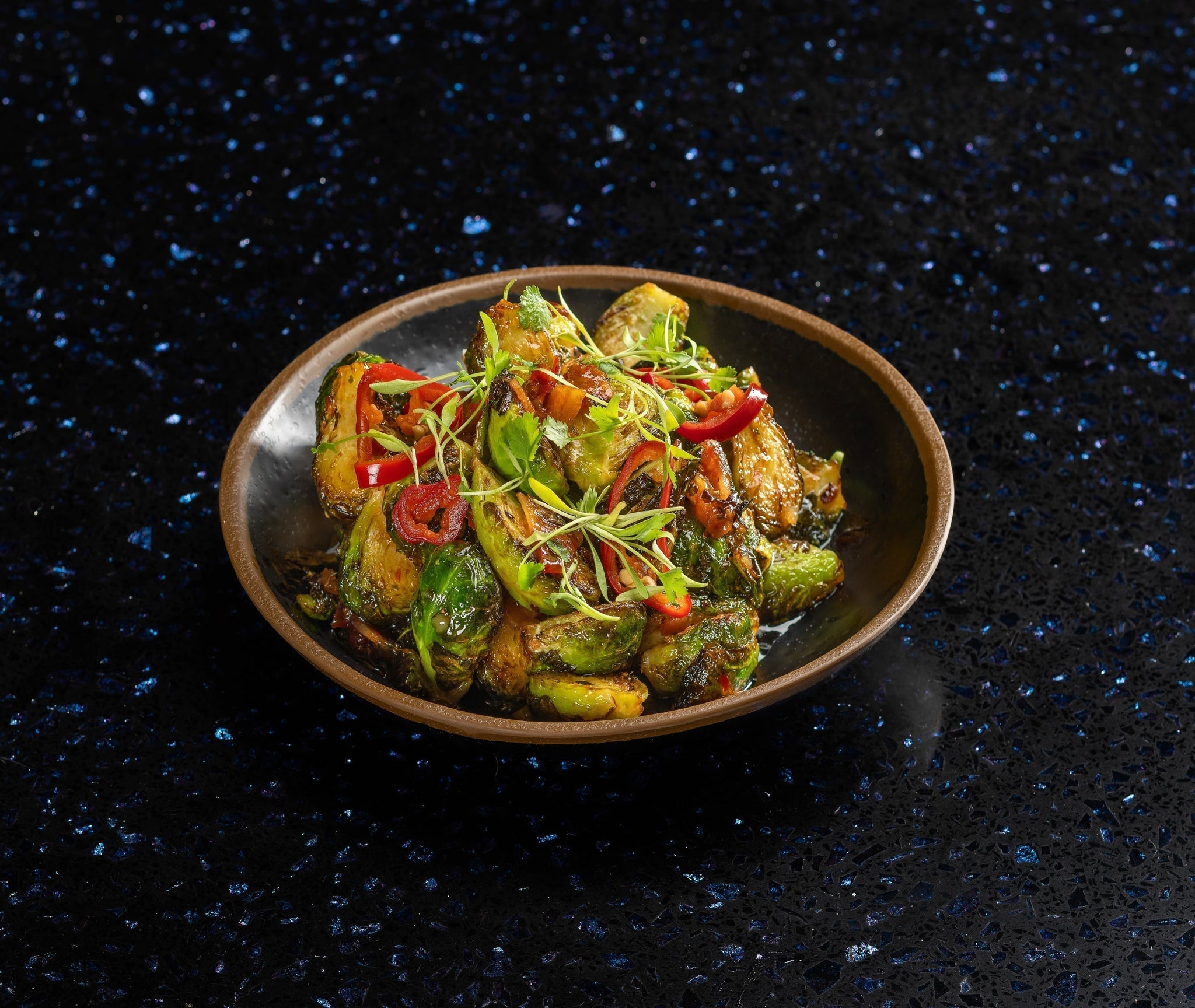 Crispy Brussels sprouts with smoky bacon, charred edges, and a drizzle of sweet heat glaze, served in a bowl.