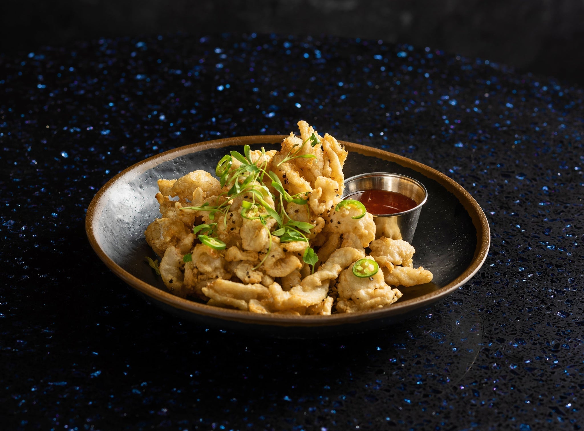Crispy fried calamari served with sweet chili sauce and pickled Fresno peppers on a plate.
