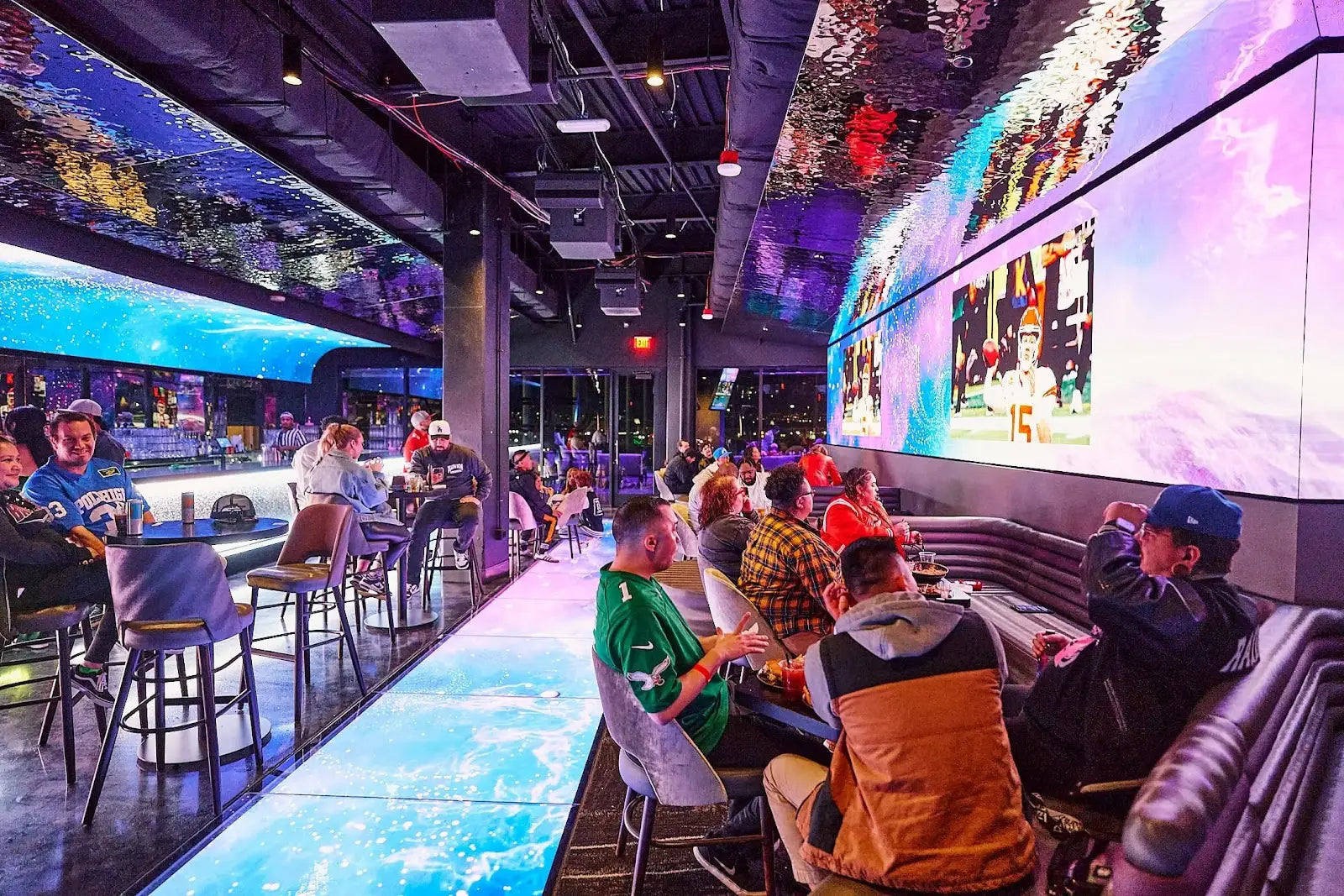 Golfer launching a ball at Atomic Golf Las Vegas under neon lights with friends cheering.