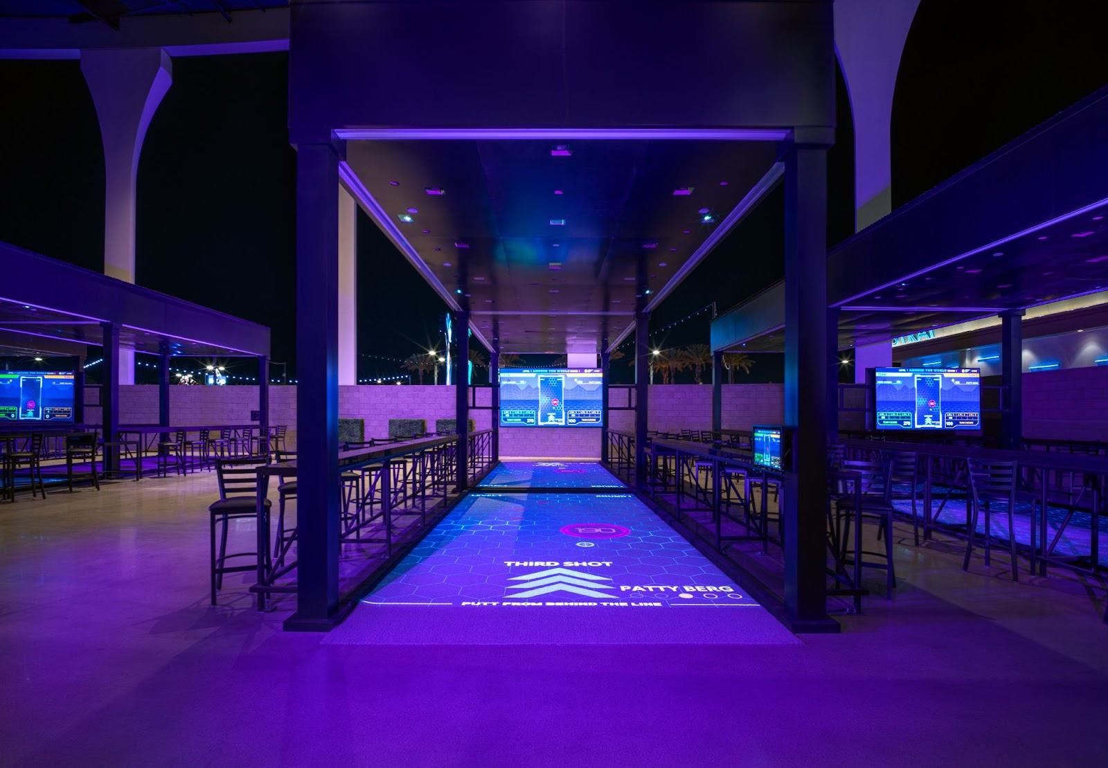 Guests enjoying a high-tech golf bay at Atomic Golf, with digital displays and a lively atmosphere.