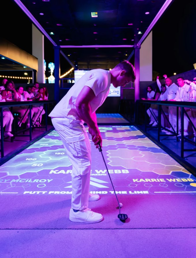  A high-tech golf bay at Atomic Golf with players enjoying interactive gameplay, food, and drinks.